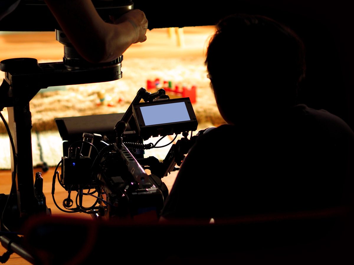 Camera operator at the director's monitor on a warm-lit set during a take